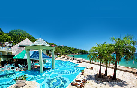 Tropical resort with pool, ocean view, palm trees, and clear blue sky.