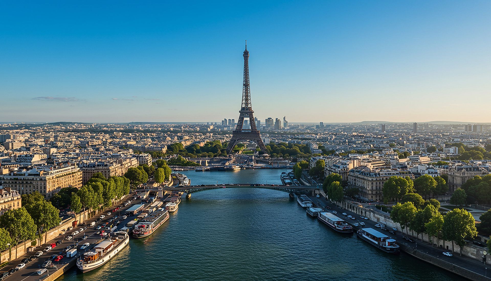 Eiffel Tower in Paris, France, rises above the city, seen from the Seine River under a bright blue sky.