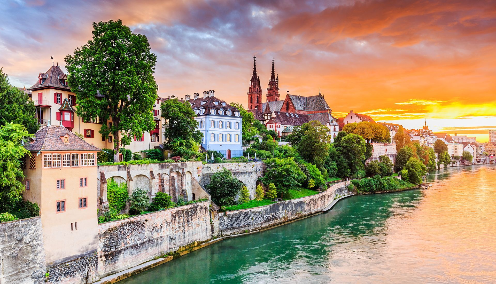 City buildings along a river at sunset with a vibrant orange sky.