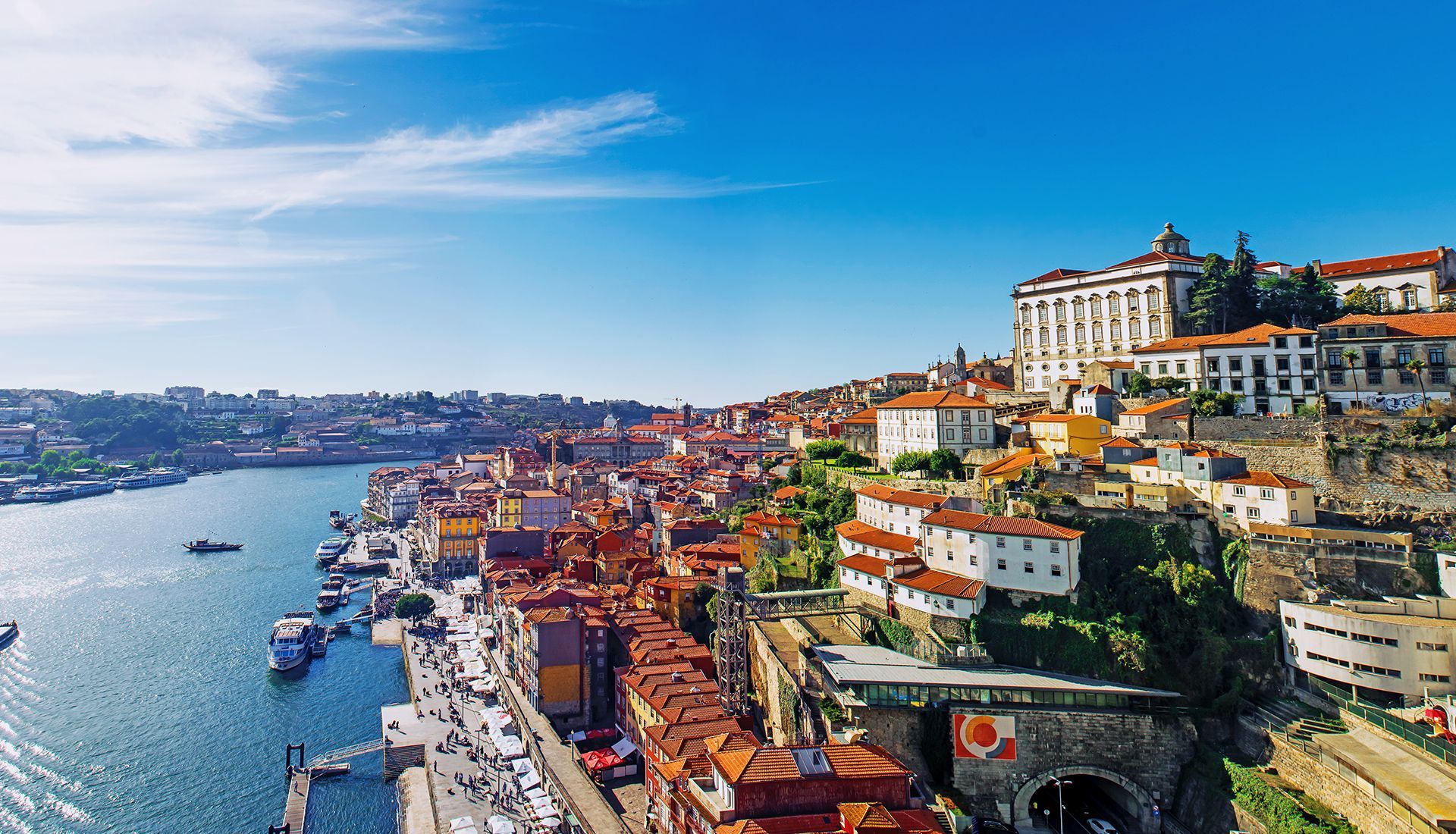 Porto, Portugal cityscape, buildings with orange rooftops along a river under a blue sky.