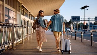 Mountains with snow-capped peaks, partially covered by clouds, overlooking turquoise water under a blue sky.