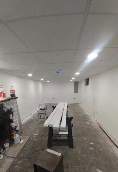 Basement interior under construction. White walls and ceiling, with work table and building materials in the center.