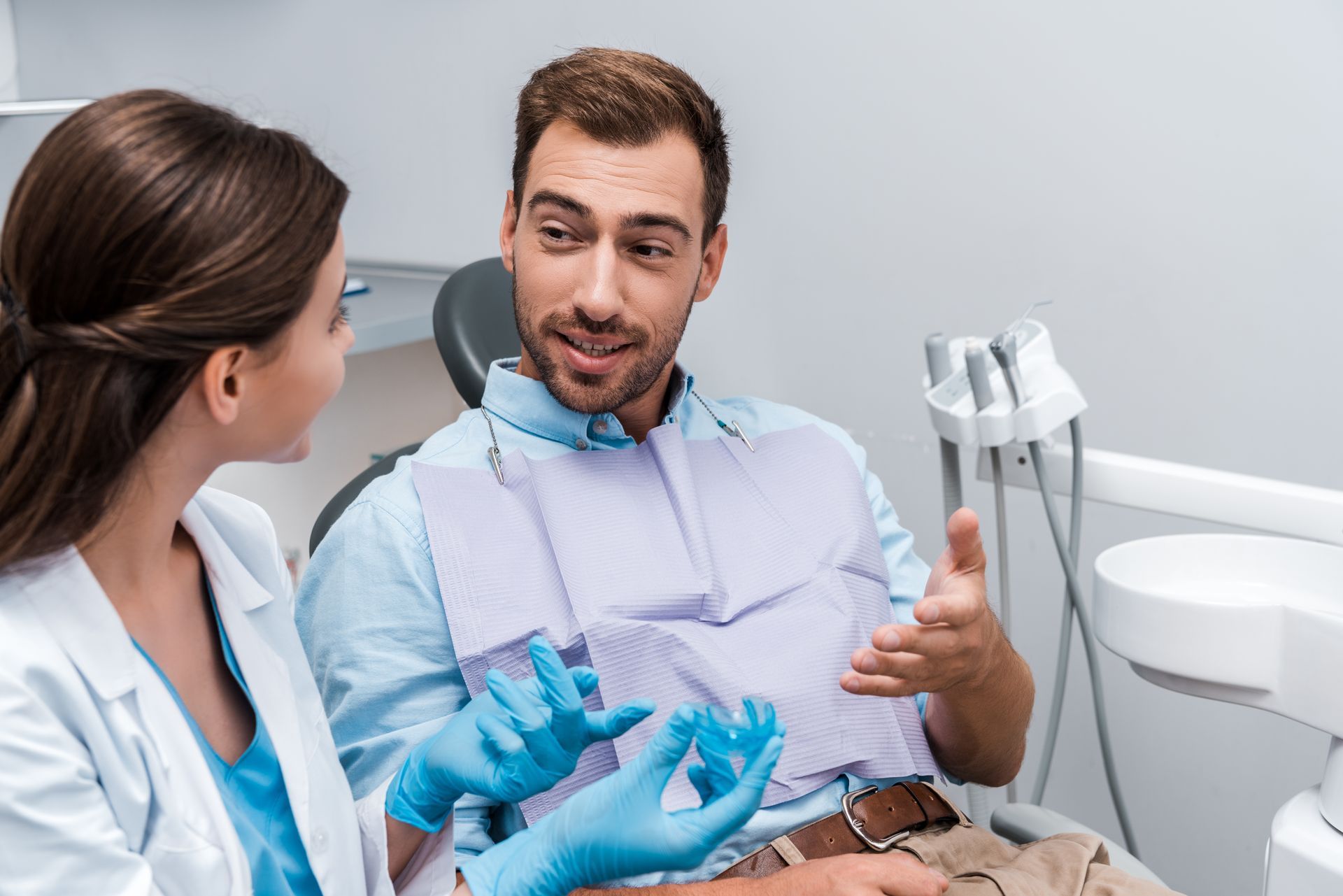 A man is sitting in a dental chair talking to a female dentist.