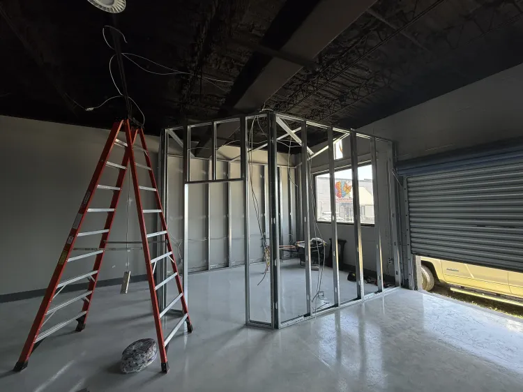 Partially built interior with exposed wall studs, a red ladder, and ceiling wiring in a room under construction