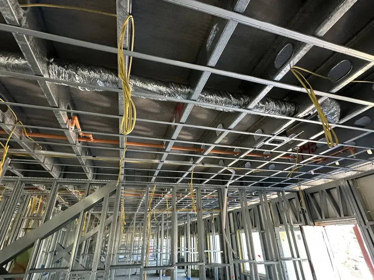 Interior construction site with exposed ceiling framing, hanging wires, and unfinished metal wall studs