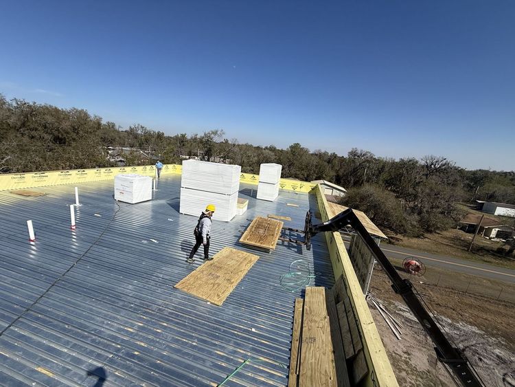 Roof under construction with workers installing silver insulation panels on a sunny day