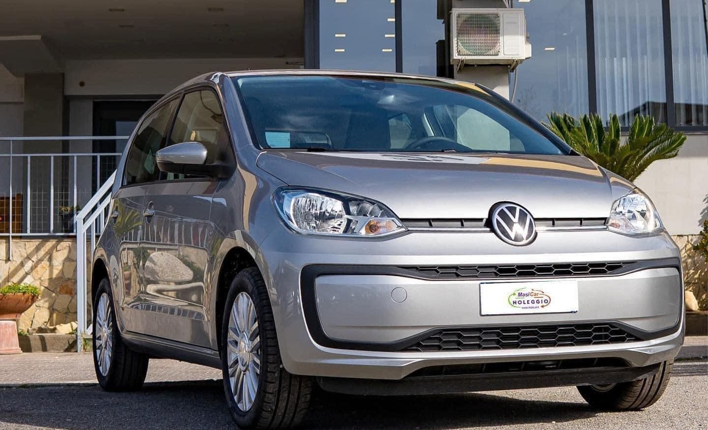 Una Volkswagen Up argentata è parcheggiata davanti a un edificio.