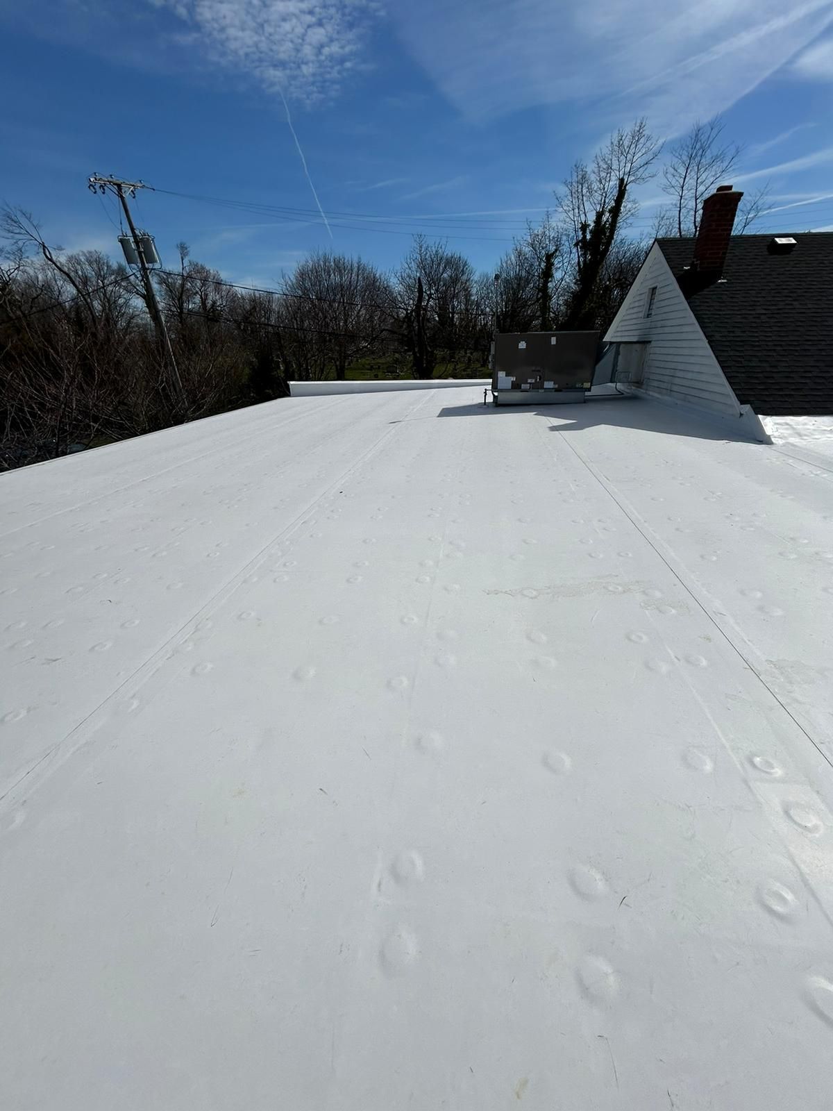 White flat roof with footprints, blue sky, trees, and a small building with a chimney.