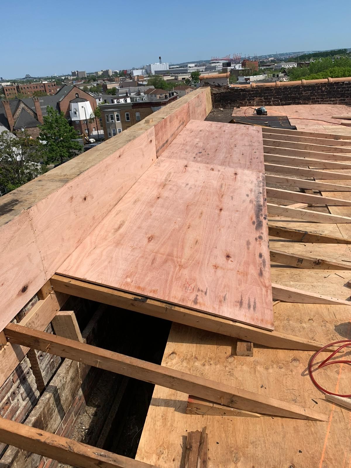 Rooftop under construction: plywood planks cover open area, wooden beams, brick walls, city background.