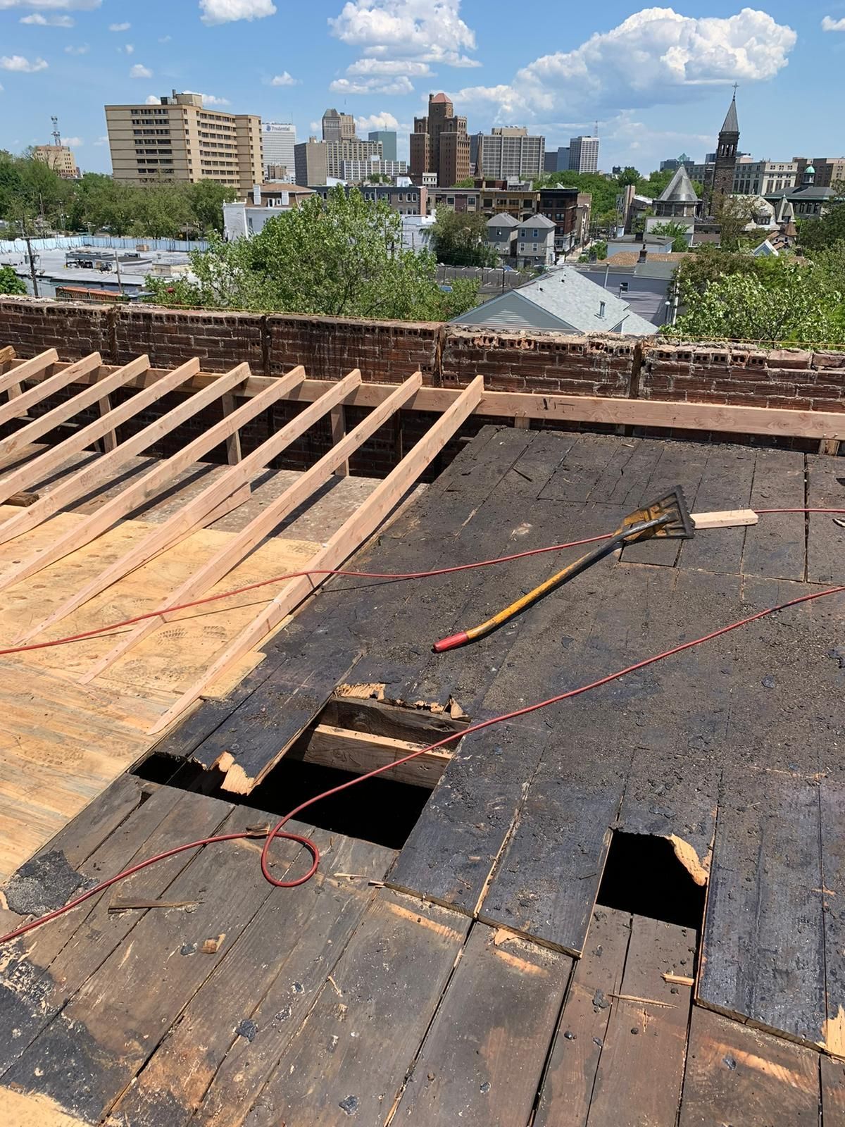 Roof partially under construction with exposed wood beams, a cityscape visible in the distance on a sunny day.