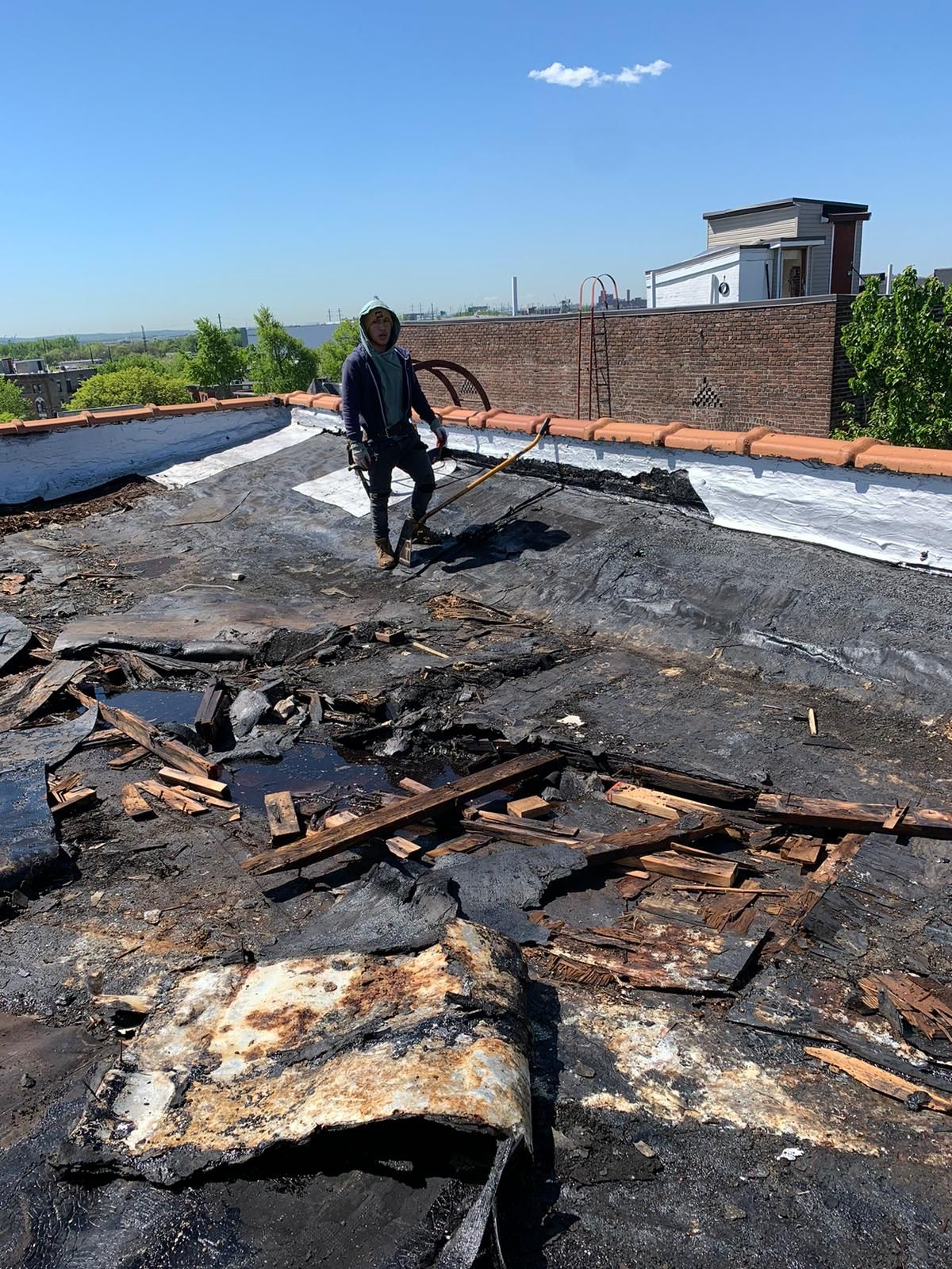 Person on a damaged black rooftop, holding a bicycle. Buildings and trees in the background.