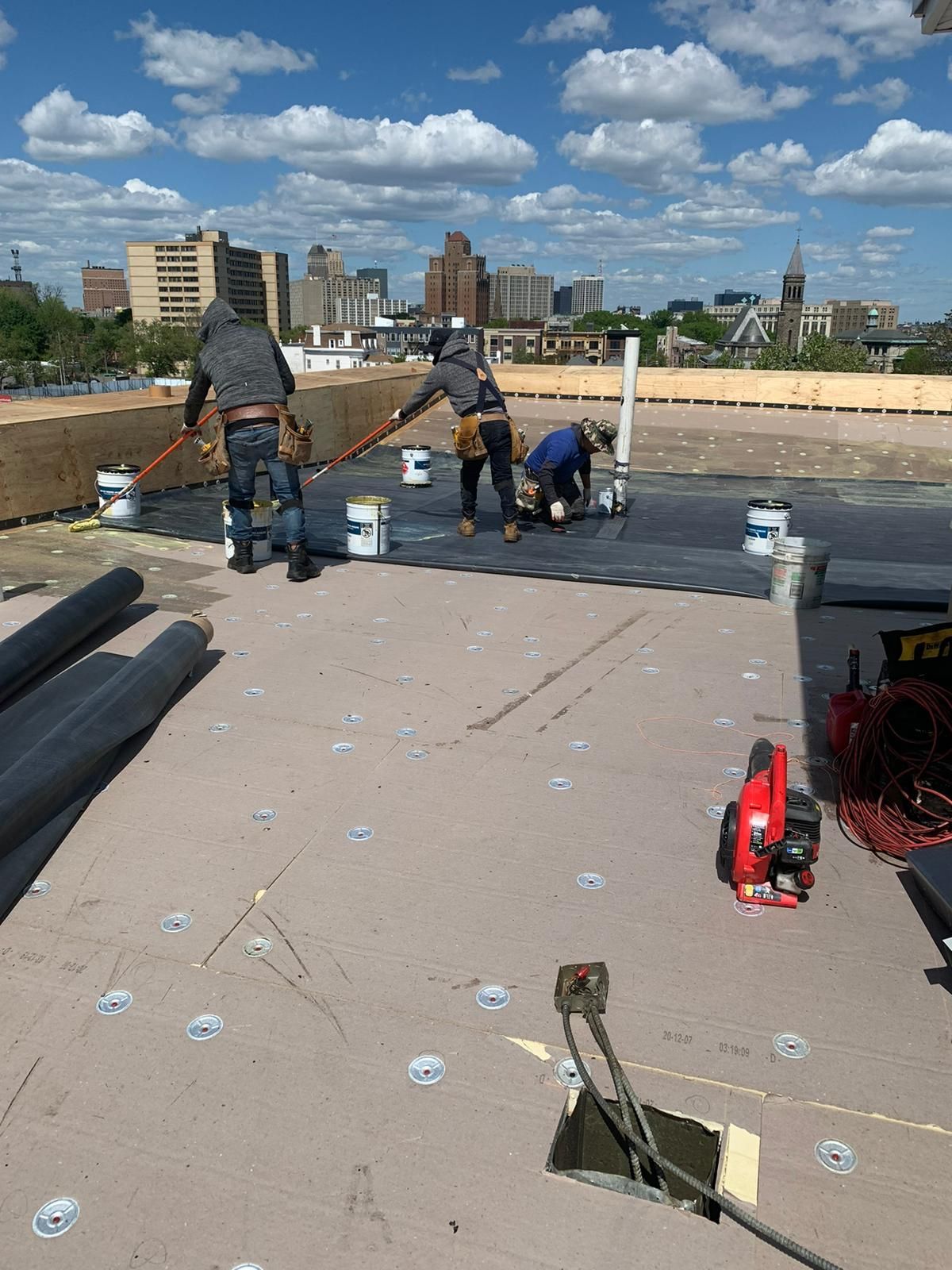 Roofers working on a flat roof in a city, applying sealant. Blue sky, sunny day.