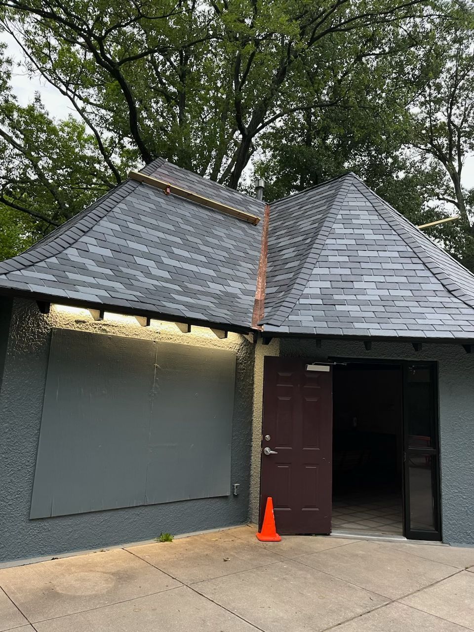 Gray building with a brown door and slate roof, orange traffic cone in front.