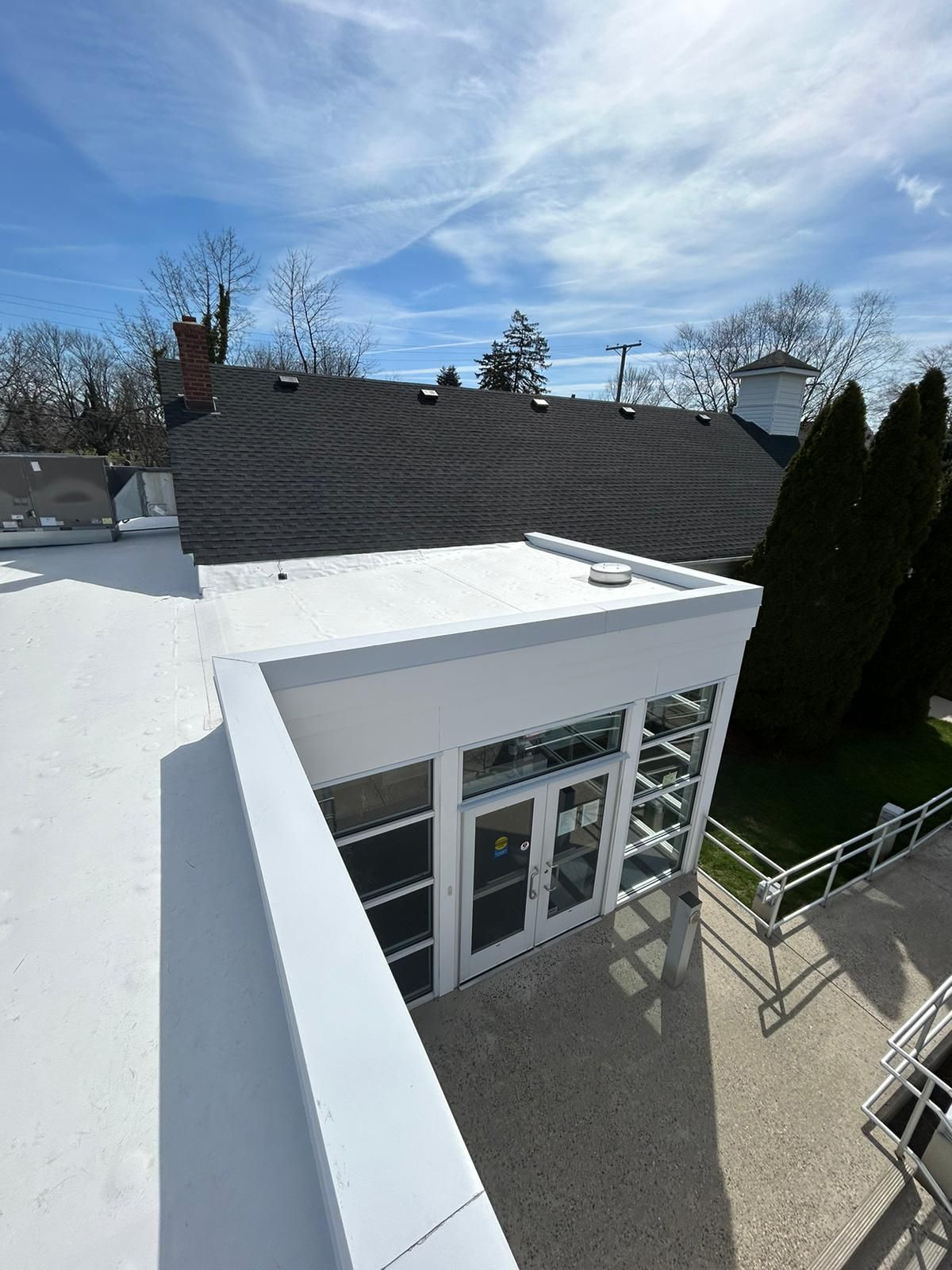 View from a white rooftop of a modern building with glass doors, black roof in background under blue sky.