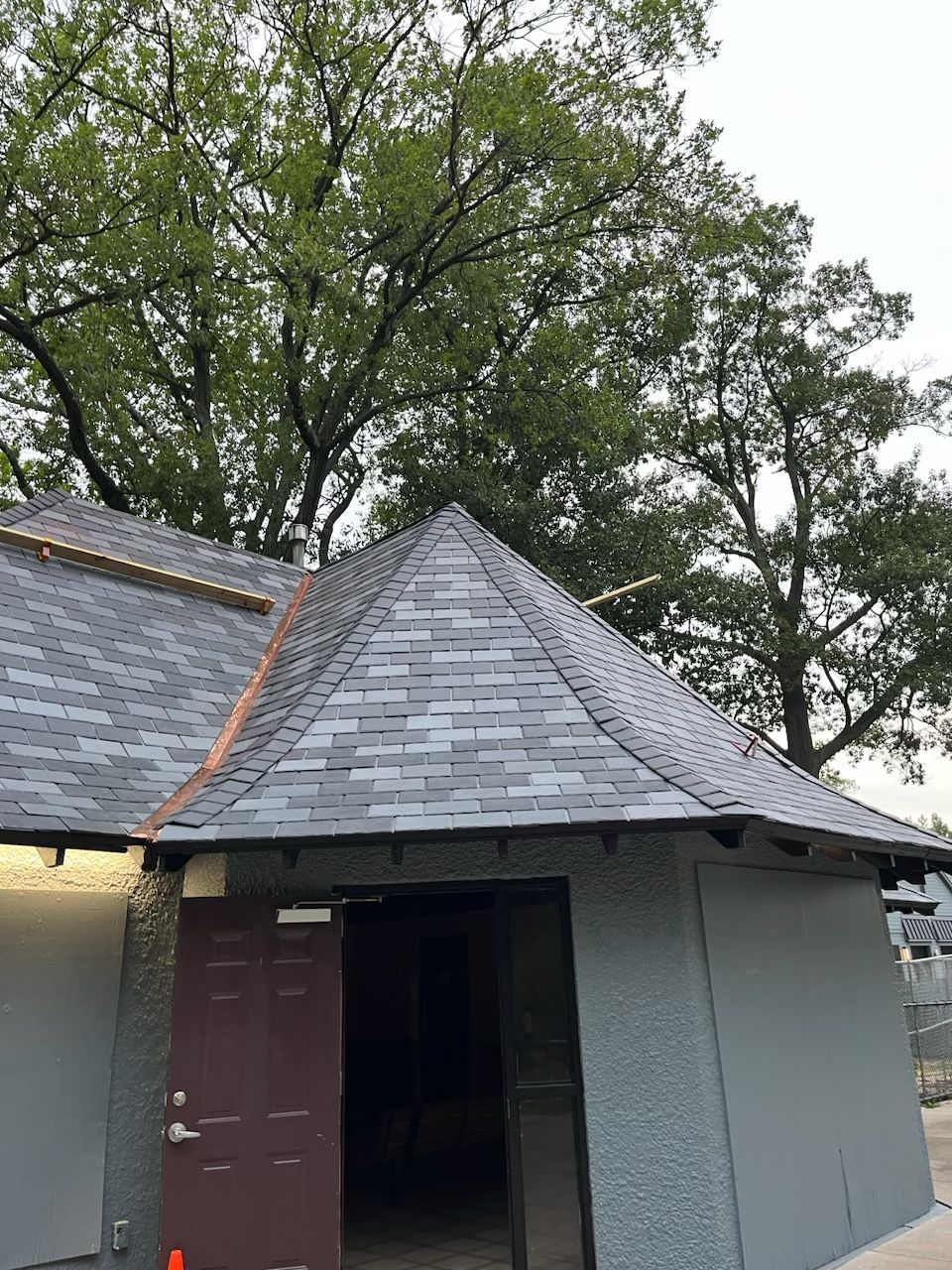 Gray building with a pyramidal roof, open doorway, and tree background.