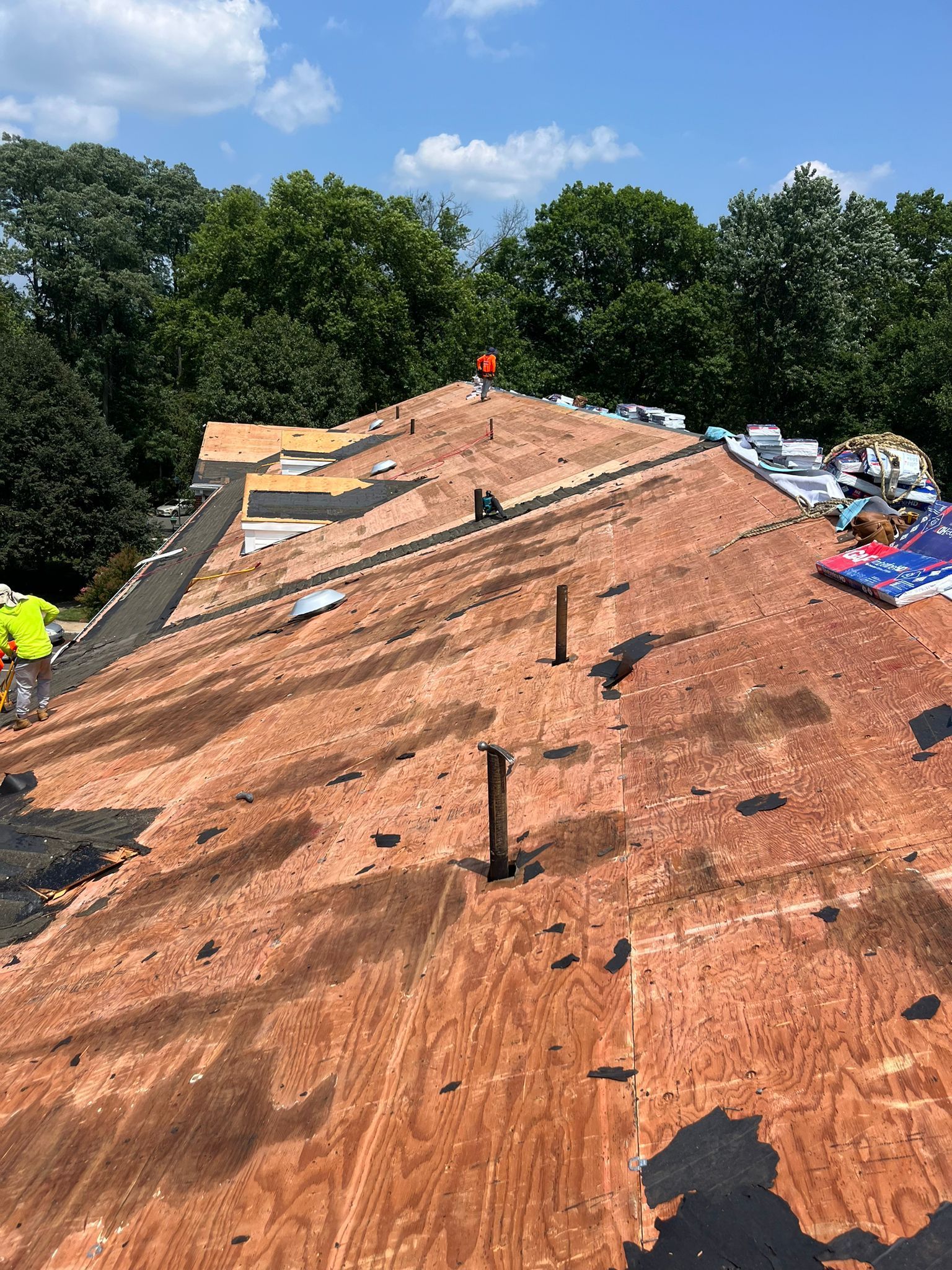 Roof being repaired, plywood exposed, workers present on a sunny day.