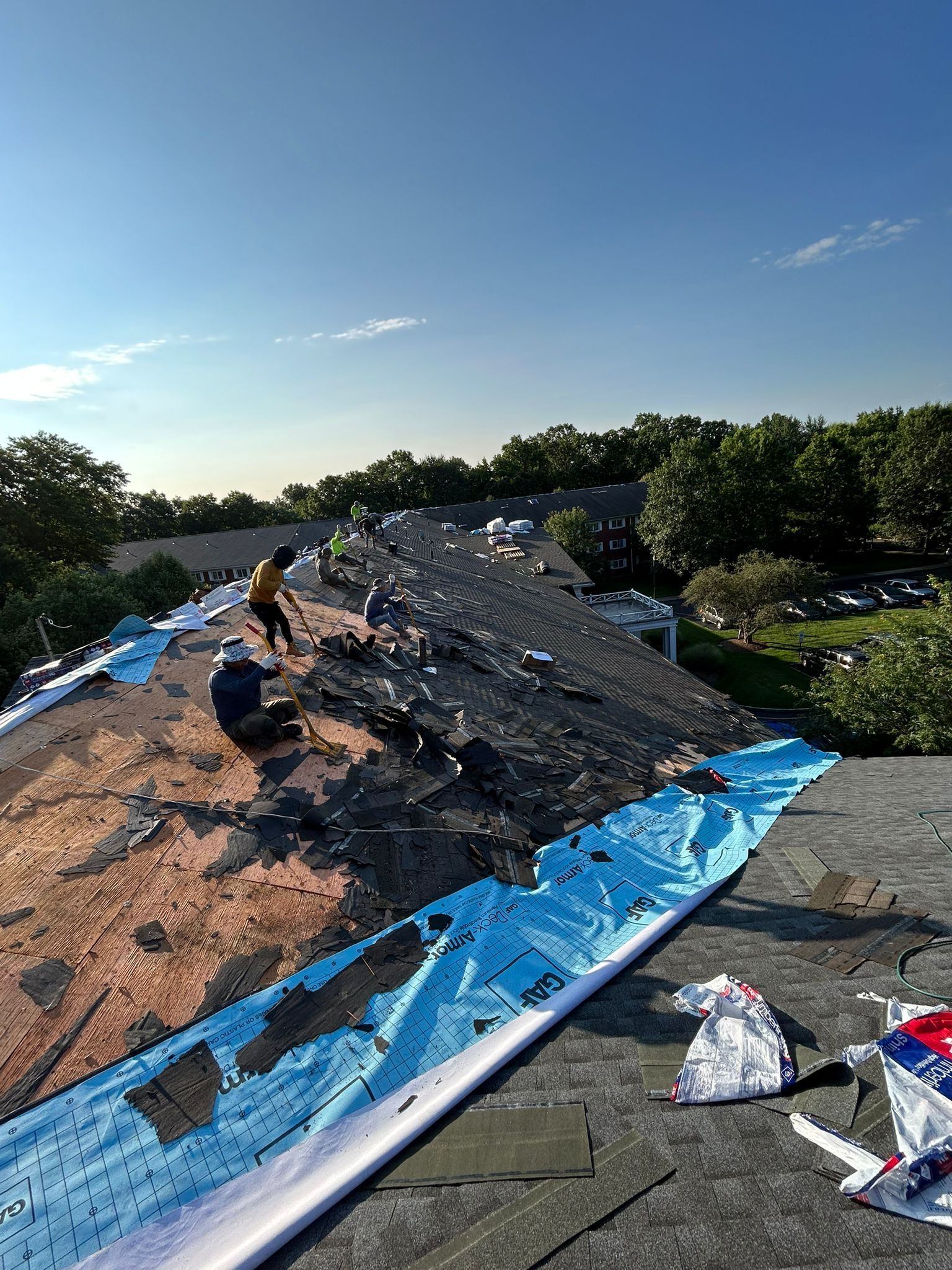 Workers removing shingles from a roof under a blue sky.