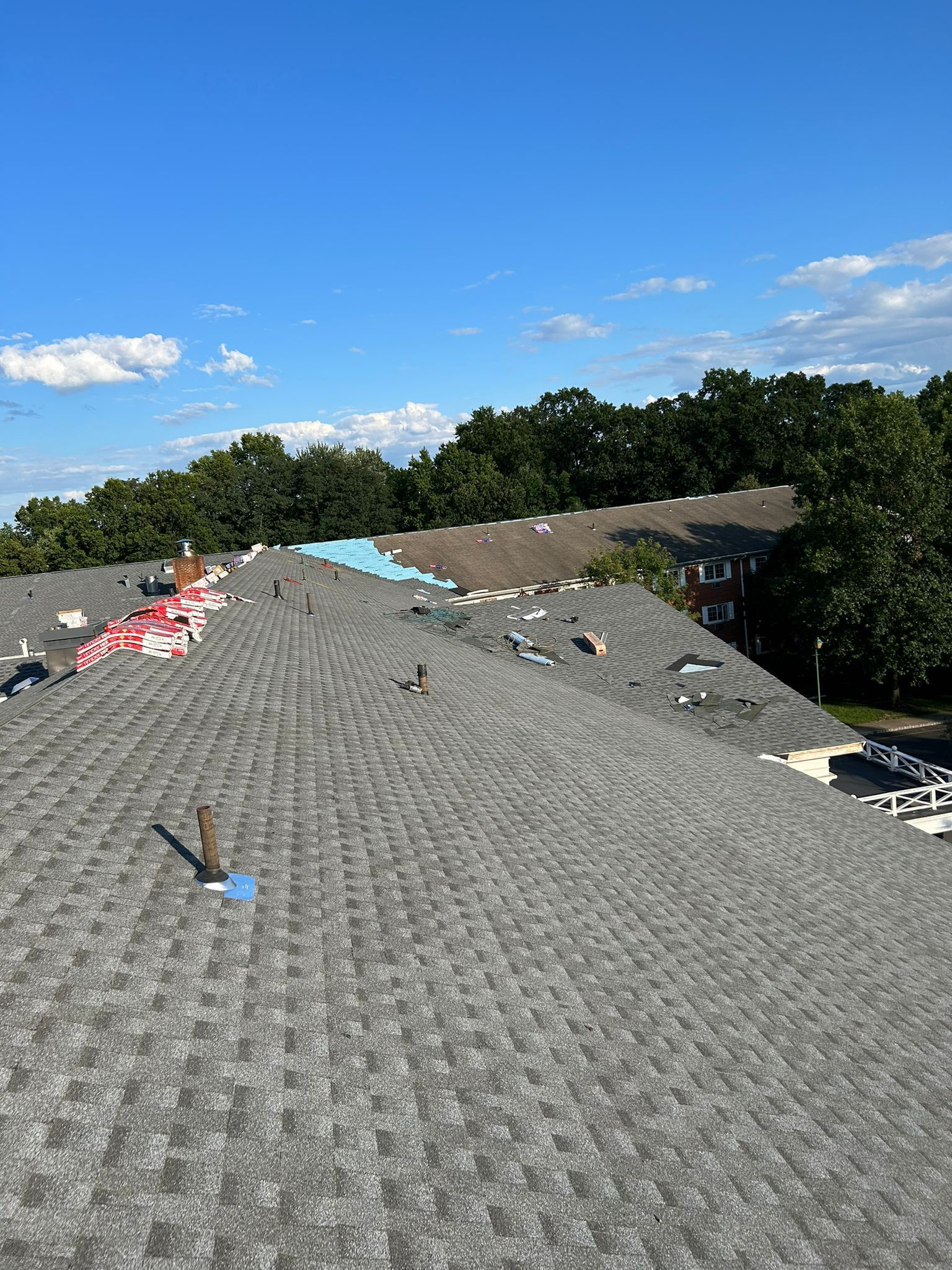 Rooftop with partial shingle replacement. Blue sky, trees in background.