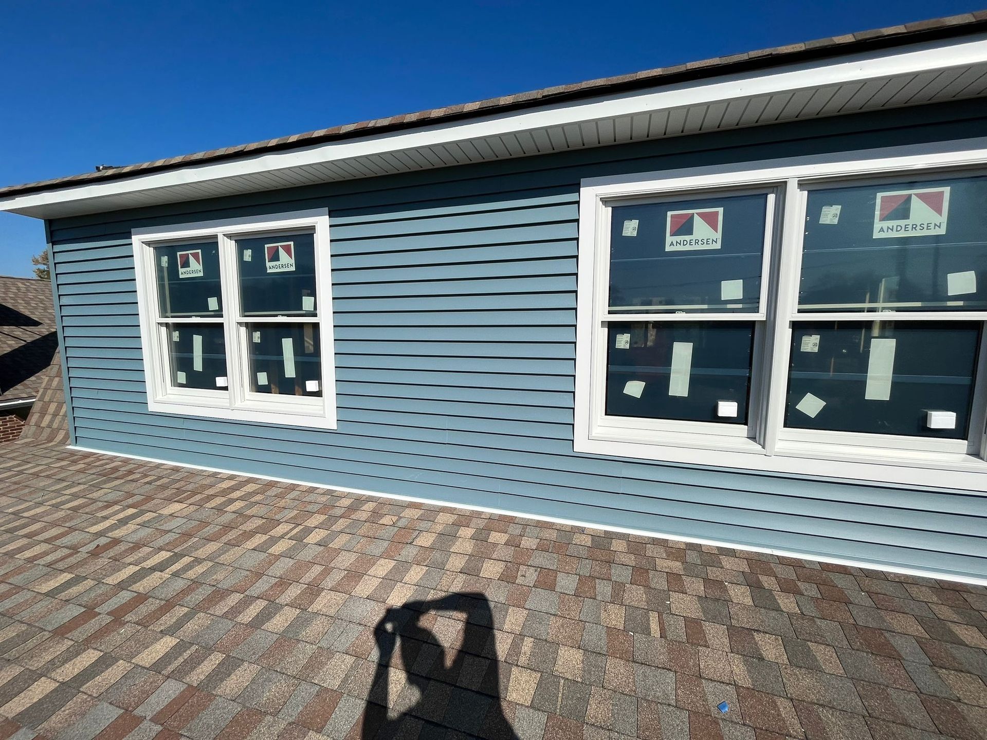 Blue siding on a house with white-framed windows; a shadow of a person is in the foreground.