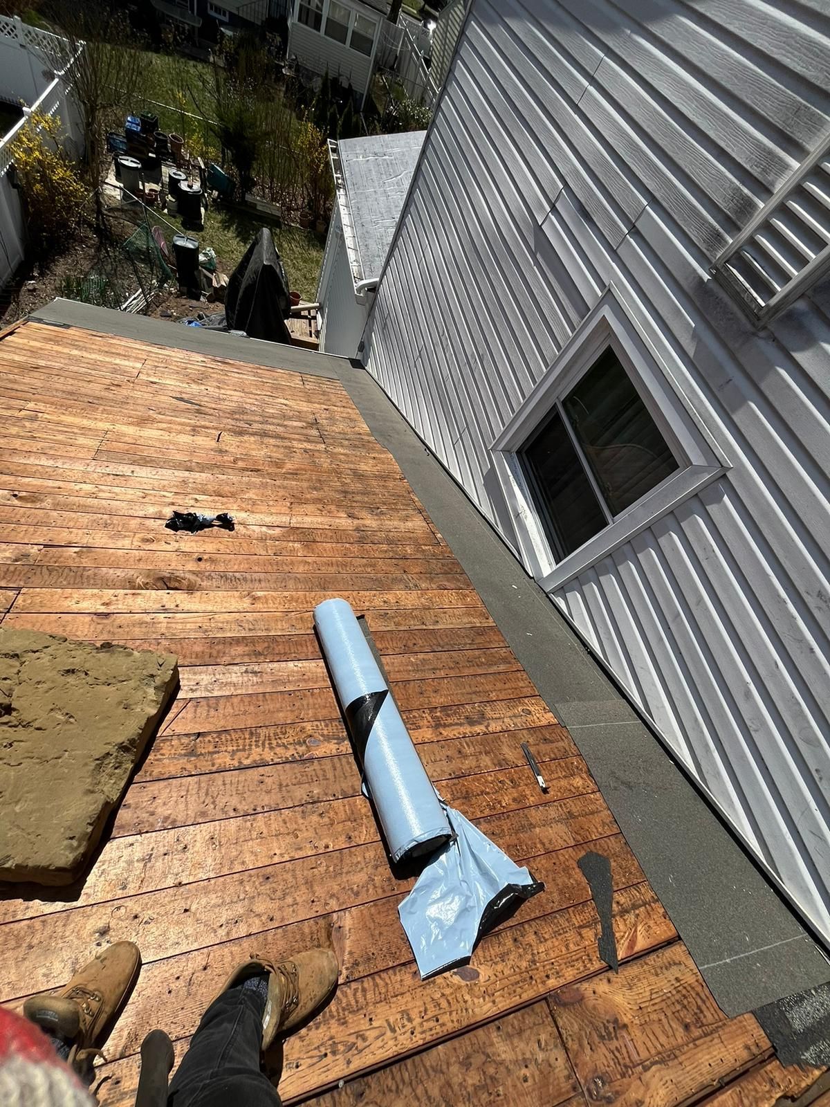 A roof being worked on, with exposed wood, metal siding, and a roll of underlayment.