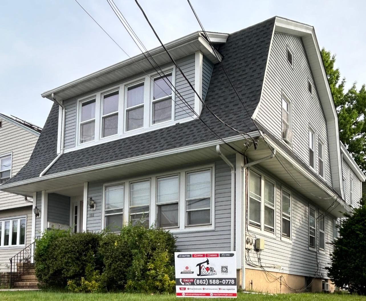 Two-story house with gray siding, dark roof, and a sign in the front yard.