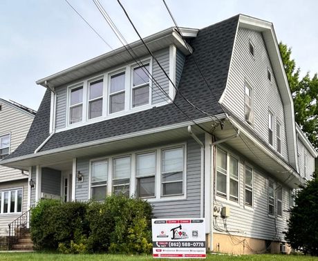 Two-story house with gray siding, dark roof, and a sign in the front yard.