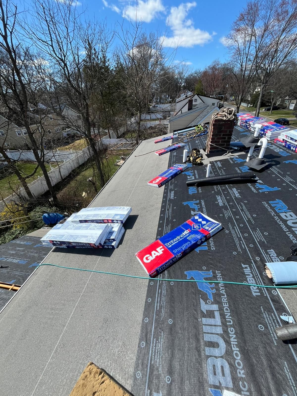 Roofing materials on a roof, including shingles, underlayment, and chimney, on a sunny day.