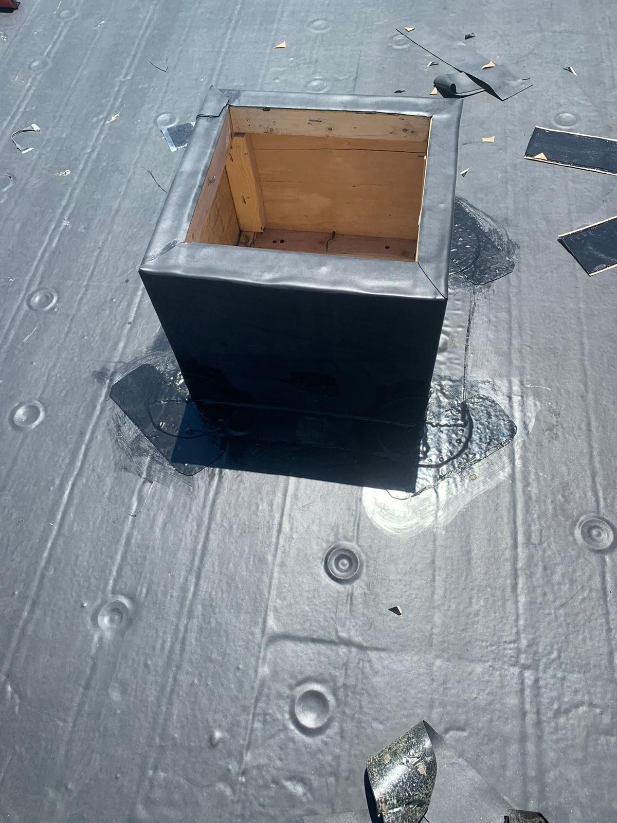 A square wooden structure sealed with black rubber on a flat, black roof.
