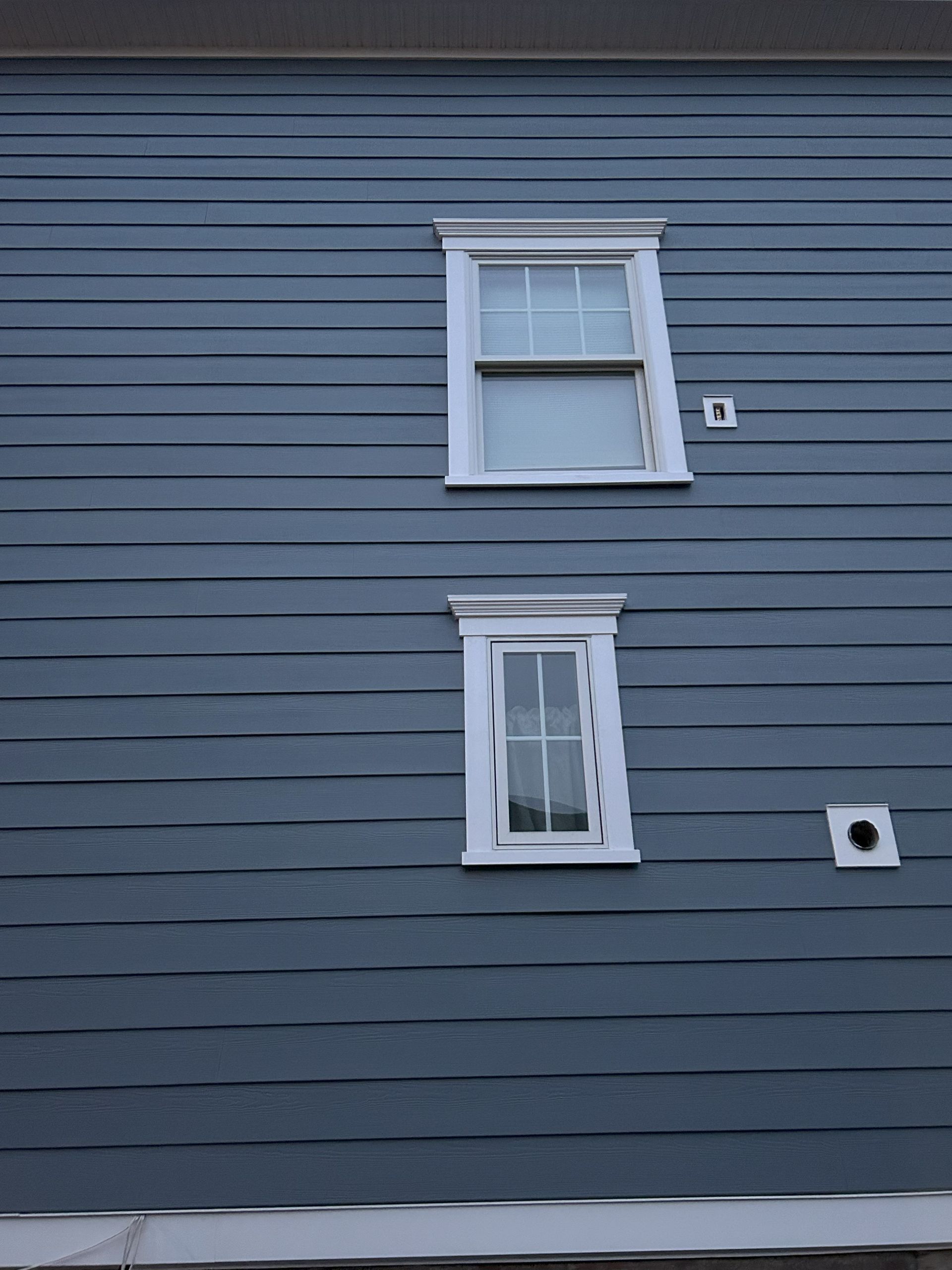 Two white-framed windows on a blue horizontal-planked building exterior; electrical outlets present.