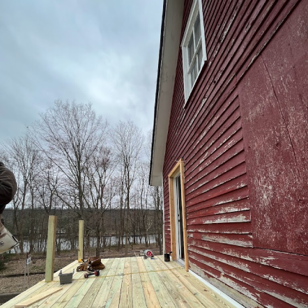 Wooden deck under construction next to a red building; cloudy sky, bare trees in the background.