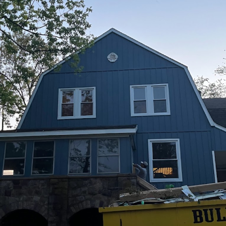 Blue house with white-framed windows, stone foundation, and a yellow dumpster below.