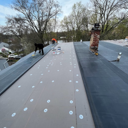 Roofers installing a flat roof, using gray and black materials, white fasteners, and working outdoors.