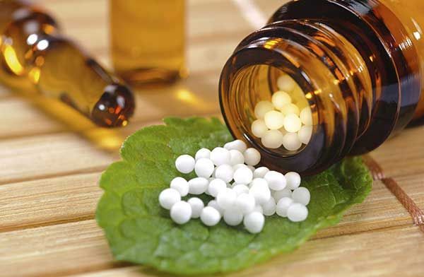 Un frasco de pastillas de homeopatía derramándose sobre una hoja.