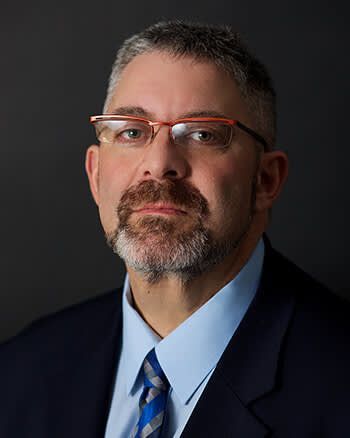 A man with a beard and glasses is wearing a suit and tie.