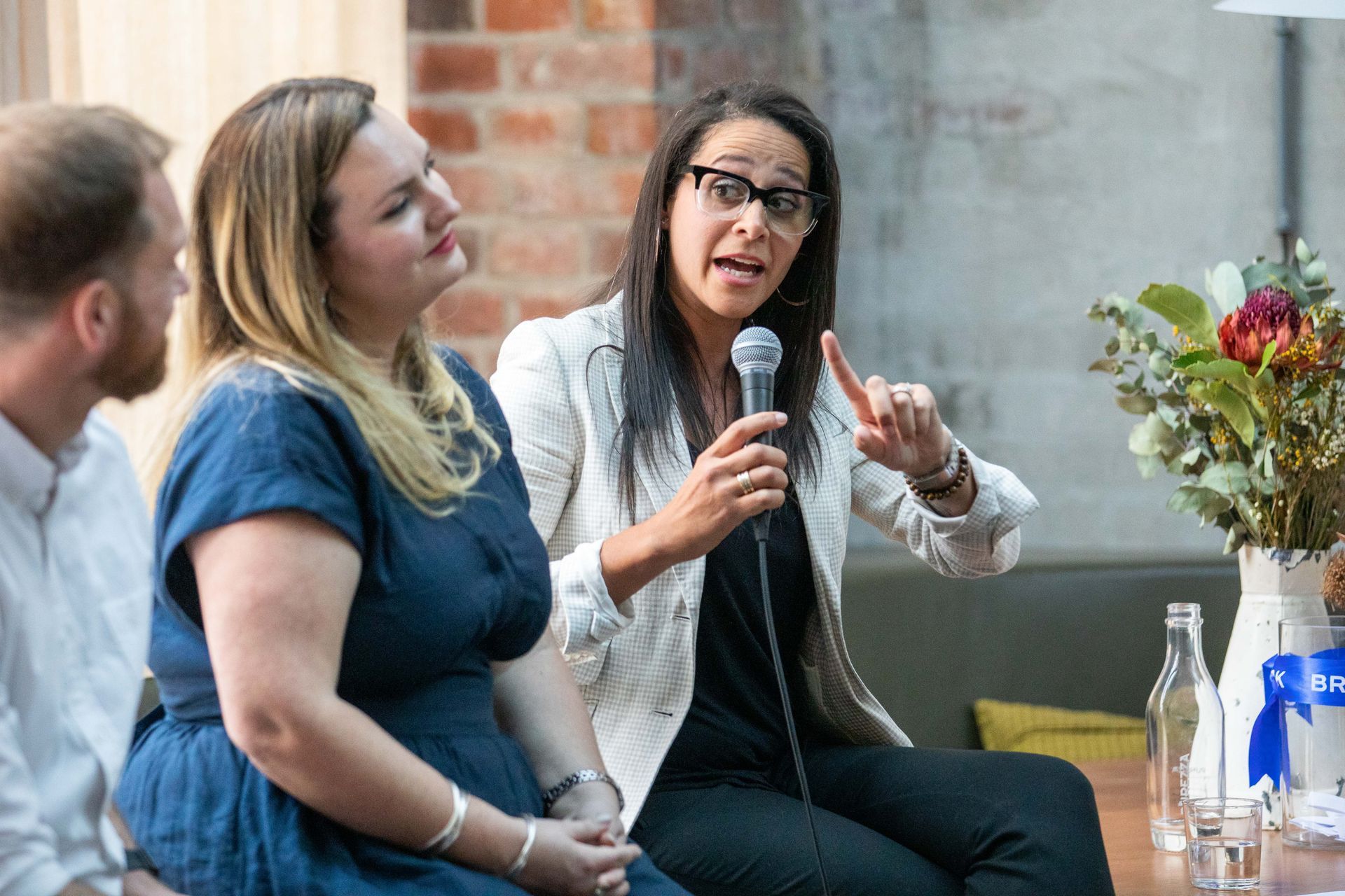 A woman is talking into a microphone while sitting at a table with two other people.