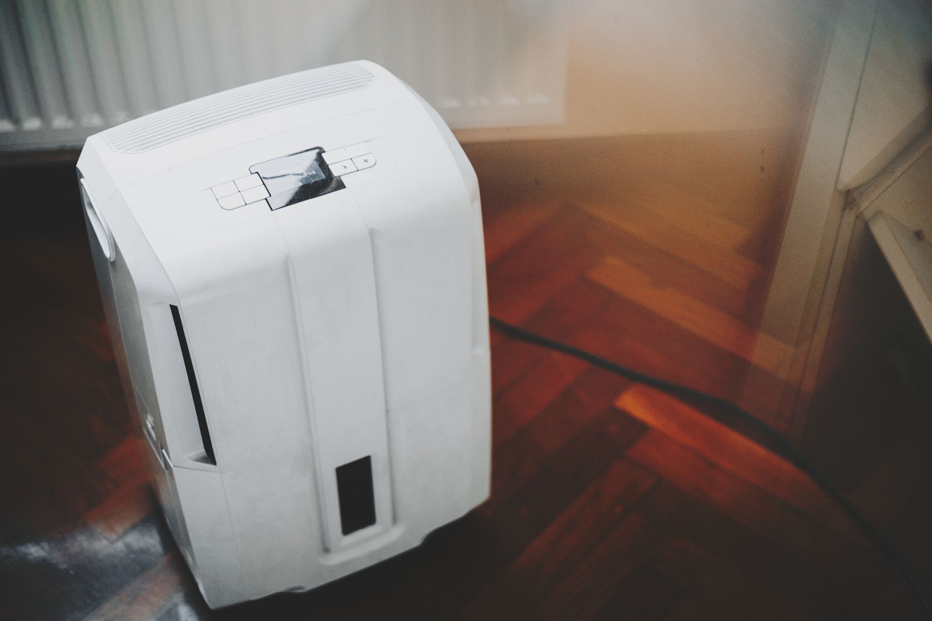 Modern portable dehumidifier system in front of a heater on hardwood floor