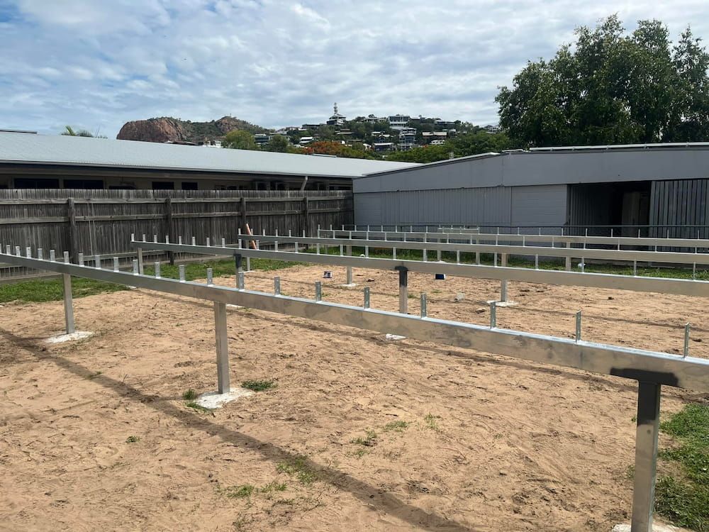 A Metal Fence Is Being Built In A Dirt Field In Front Of A Building — Quality Fabrications & Welding Pty Ltd In Bohle, QLD