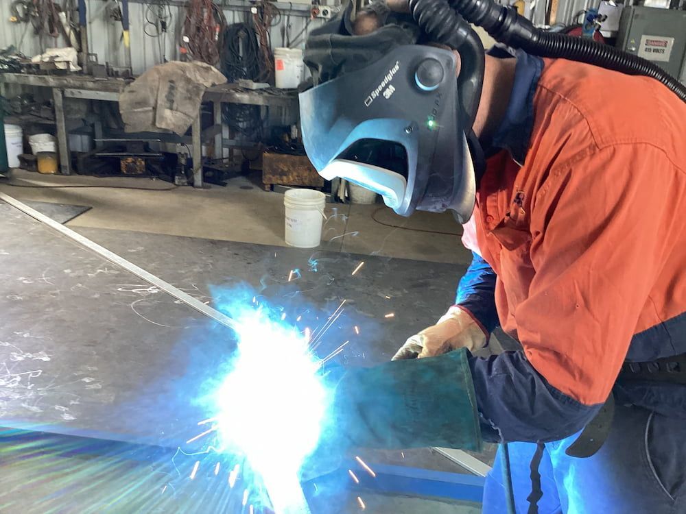 A Man Wearing A Welding Mask Is Welding A Piece Of Metal — Quality Fabrications & Welding Pty Ltd In Bohle, QLD