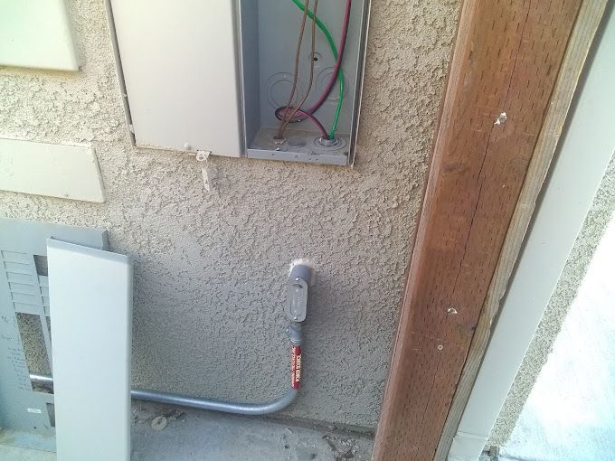 A box with wires coming out of it is on the side of a building.