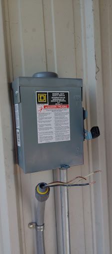 A electrical box is hanging on a wall next to a pipe.