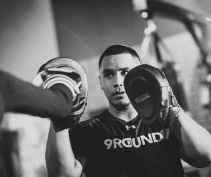 Boxer holding pads, focused, in a 9Round gym.