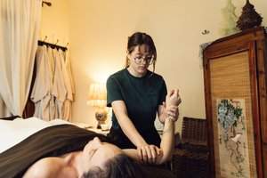 Person giving a hand massage to someone lying on a bed in a warmly lit room