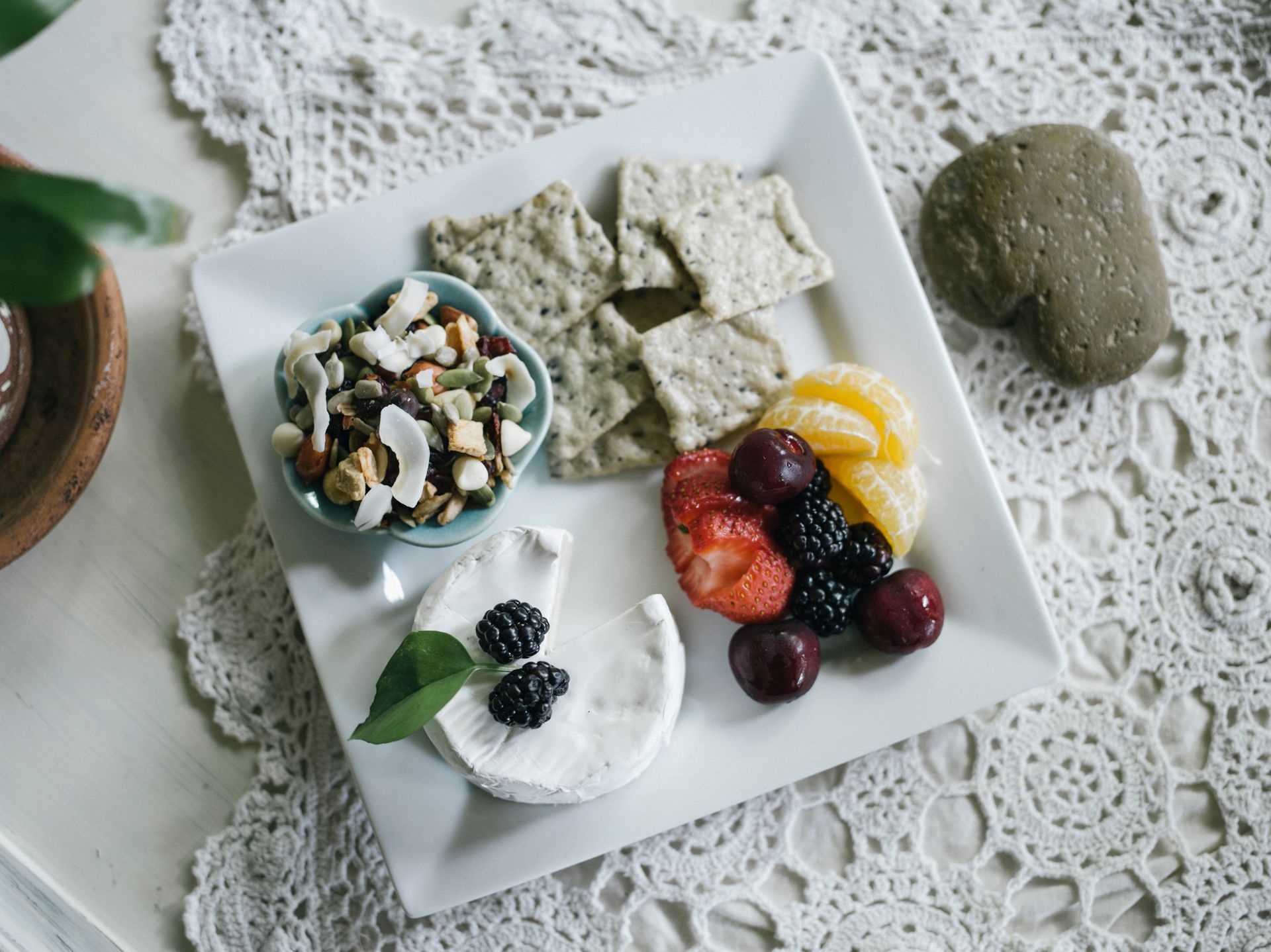 Assorted fruit, yogurt, granola, and crispbread on a white plate and lace tablecloth