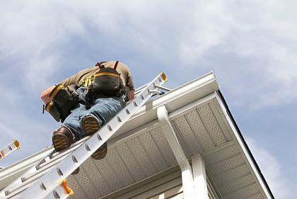 A man is standing on a ladder on the roof of a house.