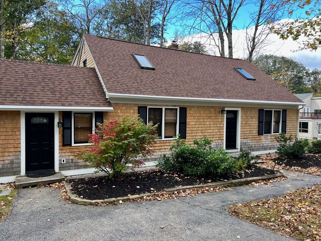 A house with a brown roof and black shutters is for sale.