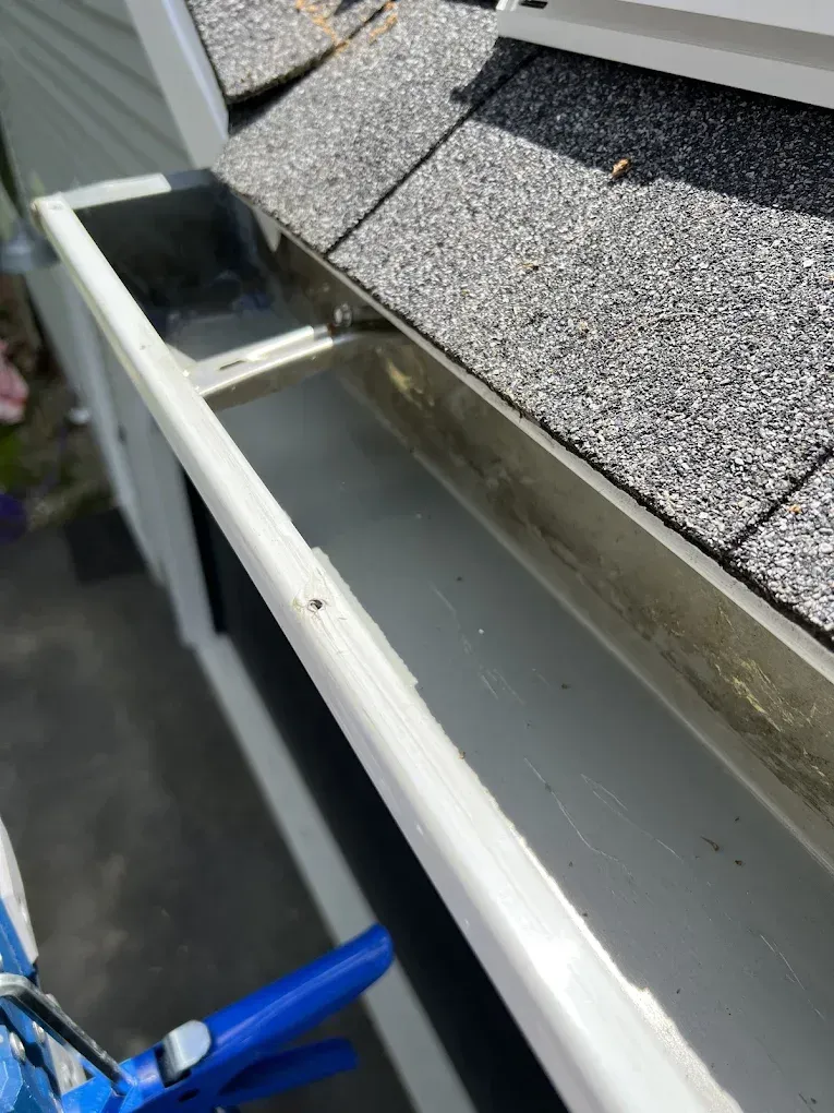 A close up of a gutter on a house with a roof in the background.