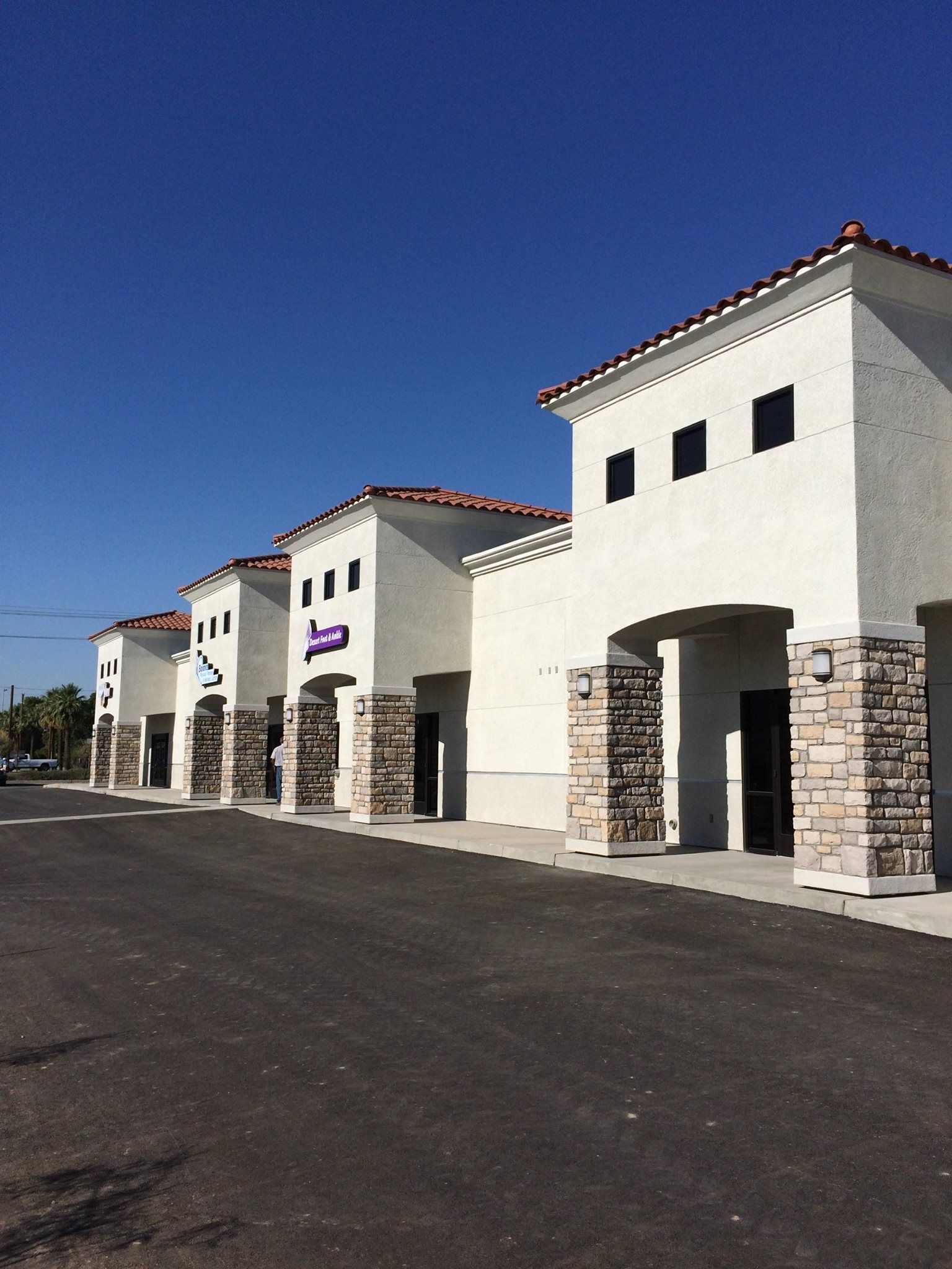 White stucco storefronts with stone columns under a clear blue sky.