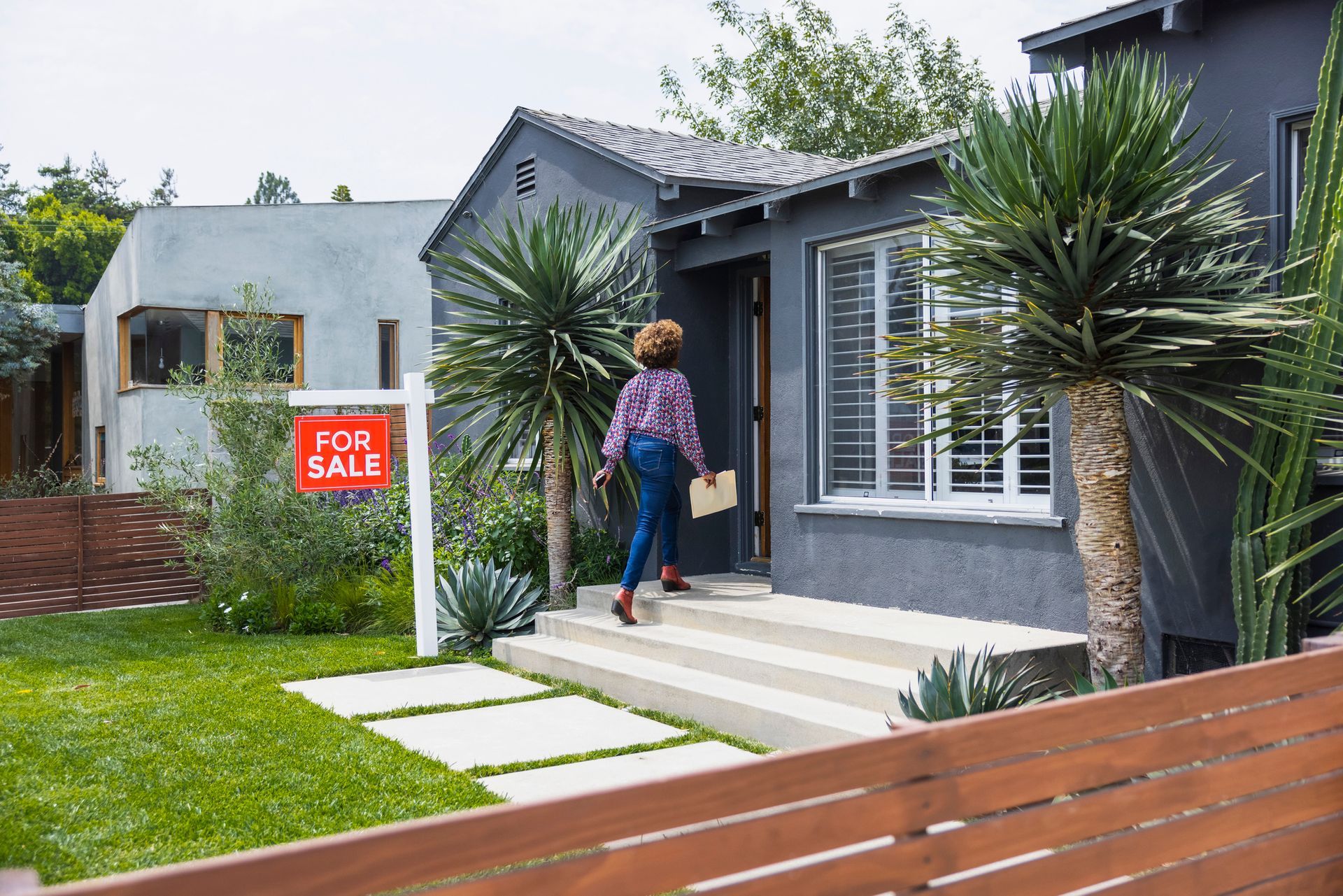 A female real estate agent carrying a document while walking into a house for sale.