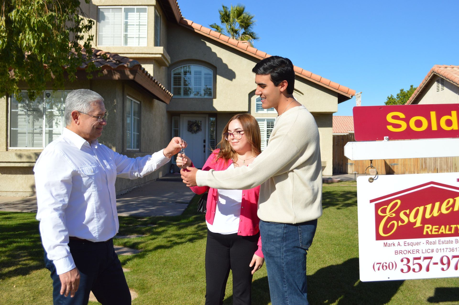 Beige stucco house with terracotta roof, arched entryway, and landscaped front yard on a sunny day.