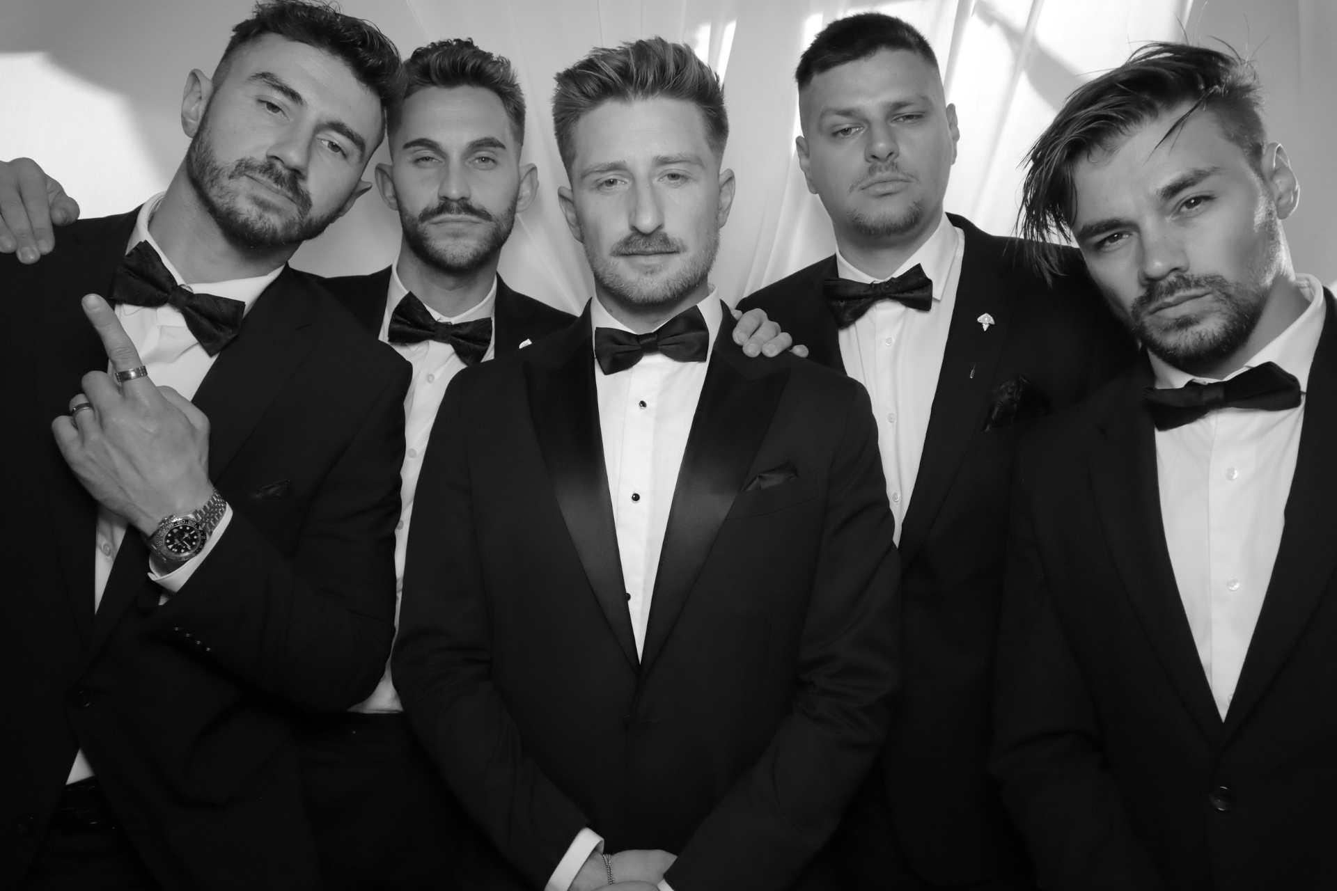A group of men in tuxedos and bow ties are posing for a picture.